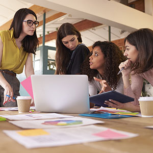 A group of women looking at a laptop - Serving Immigrants