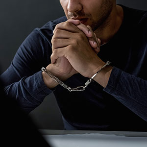 A man in handcuffs sitting at a desk - Serving Immigrants