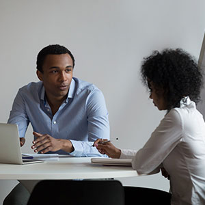 A man and woman sitting at a table with a laptop - Serving Immigrants