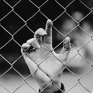 Hand holding a chain link fence - Serving Immigrants