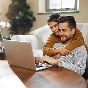 A couple sitting together on a sofa, using a laptop - Serving Immigrants