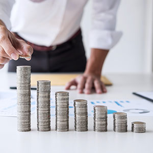 A man putting a coin on a stack of coins - Serving Immigrants