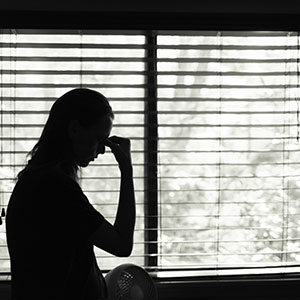 A women holding her hand to her face in front of window - Serving Immigrants