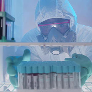 A man in a protective suit looking at test tubes - Serving Immigrants