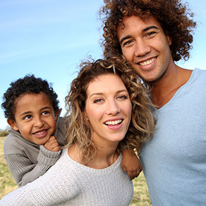 A couple with their child in a grassy field - Serving Immigrants