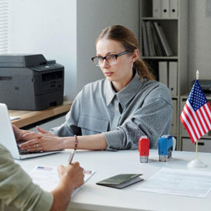 A man and woman sitting at a desk with an American flag - Serving Immigrants